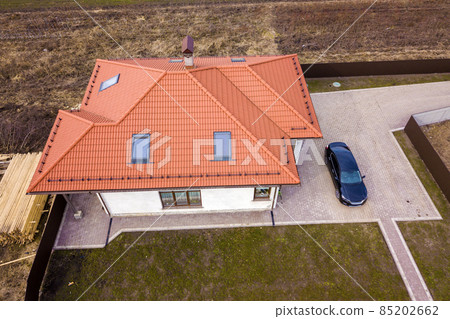 Aerial top view of house metal shingle roof with attic windows and black car on paved yard. Aerial top view of house metal shingle roof with attic windows and black car on paved yard. 85202662