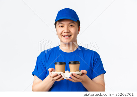 Online orders, takeaway and employees concept. Handsome smiling asian delivery man in blue courier uniform, handing coffee to customer and looking friendly, standing white background Online orders, takeaway and employees concept. Handsome smiling asian delivery man in blue courier uniform, handing coffee to customer and looking friendly, standing white background 85202701