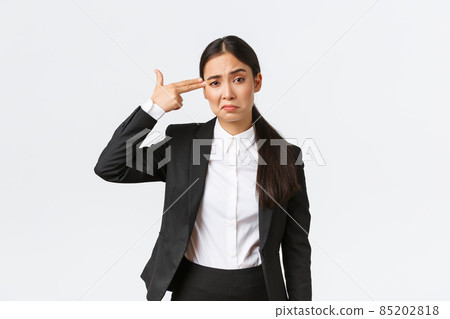 Just shoot me please. Bothered and fed up asian saleswoman hate her work, standing in business suit, shooting herself with hand gun gesture as feeling exhausted, standing white background 85202818
