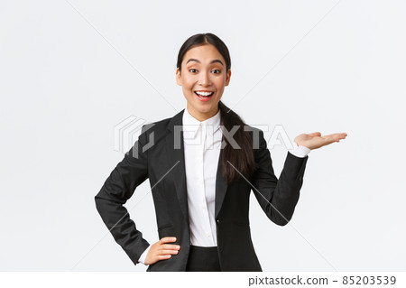 Excited smiling saleswoman introduce product, trying sell something over white copyspace. Pretty asian female manager showing project, pointing hand right and looking upbeat, white background 85203539