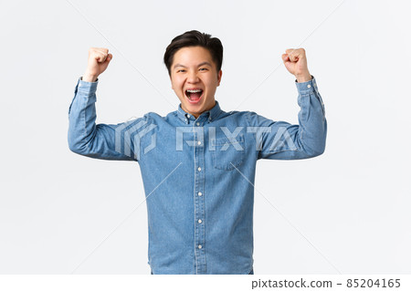 Excited happy asian man with braces feeling success over winning prize, fist pump and shouting yes, rejoicing, triumphing as becoming champion, standing white background celebrating 85204165