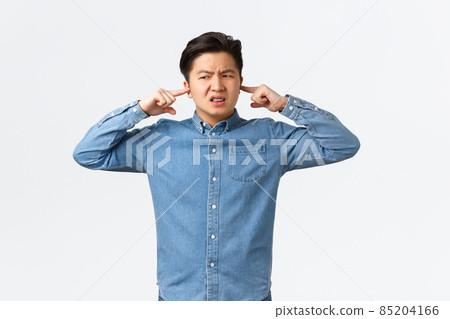 Disturbed and frustrated asian man complaining loud noise, shut ears and looking left displeased, frowning upset, telling neighbour be quiet, college student cant focus because of noisy awful music 85204166