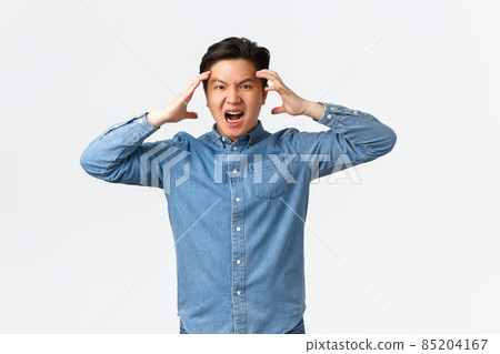 Mad and distressed asian man looking furious and frustrated, losing temper, holding hands on head and frowning angry, losing control over emotions, feeling anger and rage, white background 85204167