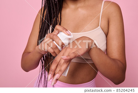 Close-up of a woman in beige underwear applying moisturizer on her hand, caring for her skin. Body care, hydrating and moisturizing beauty treatment concept on pink background with copy space 85204245