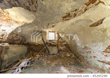 Old forsaken empty basement room of ancient building or palace with cracked plastered brick walls, low arched ceiling, small windows with iron bars and dirty floor. 85205290