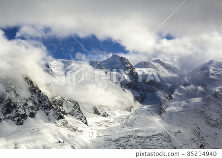 Breathtaking aerial view of Mont Blanc mountain peak covered with shiny snow, ice and glaciers under blue sky with puffy white clouds on the French side of Alps on a clear cold sunny winter day 85214940