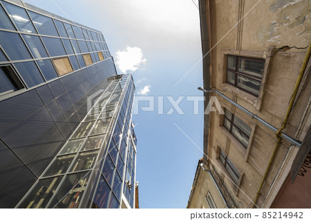 Bottom view of tall building with glass wall opposite neglected crackled plastered on blue sky copy space background. Comparison of modern and old technologies and lifestyles, past and future. Bottom view of tall building with glass wall opposite neglected crackled plastered on blue sky copy space background. Comparison of modern and old technologies and lifestyles, past and future. 85214942
