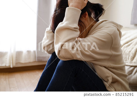 A woman sitting on the floor in a room and holding her head A woman sitting on the floor in a room and holding her head 85215291