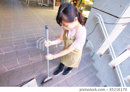 A woman in an apron sweeping a common area of an apartment with a broom A woman in an apron sweeping a common area of an apartment with a broom 85216179