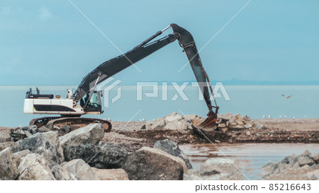 Excavator working on earthmoving at open pit mining . Bulldozer digs sand and gravel in quarry. Heavy construction equipment during excavation at construction site near a sea Excavator working on earthmoving at open pit mining . Bulldozer digs sand and gravel in quarry. Heavy construction equipment during excavation at construction site near a sea 85216643