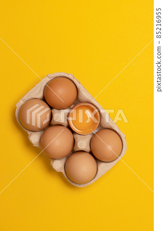 Brown chicken eggs and one broken egg with yolk in eco basket on yellow background 85216955