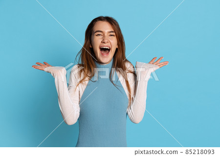 Half-length portrait of pretty girl with long glossy hair spreads her arms to side in delight isolated on blue studio backgroud. 85218093