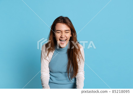 Half-length portrait of pretty girl with long glossy hair laughing isolated on blue studio backgroud. Human emotions, facial expression concept 85218095