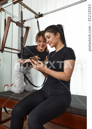 Brunette caucasian woman personal trainer during a workout session on pilates reformer bed equipment with an attractive client in light medical office. Healthy lifestyle rehabilitation concept. Brunette caucasian woman personal trainer during a workout session on pilates reformer bed equipment with an attractive client in light medical office. Healthy lifestyle rehabilitation concept. 85218563