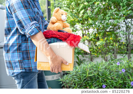 Holding clothing donation box with used clothes and doll at home to support help for poor people in the world. 85220276