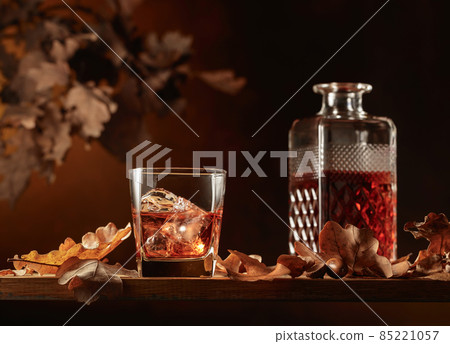 Whiskey on a wooden table with dried-up oak leaves. Whiskey on a wooden table with dried-up oak leaves. 85221057