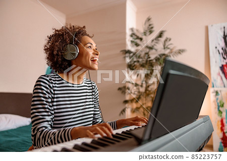 Cheerful young woman playing synthesizer at home 85223757