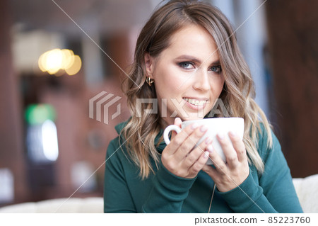 Close-up portrait of an optimistic beautiful woman with a beautiful manicure, holding a cup, sitting in a cafe, the girl looks directly into the camera. High quality photo 85223760