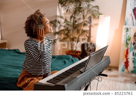 Cheerful woman in headphones playing synthesizer at home Cheerful woman in headphones playing synthesizer at home 85223761