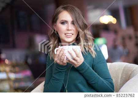 A beautiful woman with a lady's hairstyle and holding a cup of coffee is sitting in a cafe. He looks directly at the camera with a smile. High quality photo A beautiful woman with a lady's hairstyle and holding a cup of coffee is sitting in a cafe. He looks directly at the camera with a smile. High quality photo 85223762