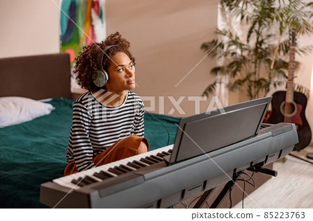 Multiracial woman sitting near synthesizer at home Multiracial woman sitting near synthesizer at home 85223763