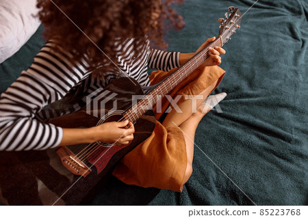 Multiracial young woman playing guitar at home Multiracial young woman playing guitar at home 85223768