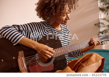 Smiling young woman playing guitar at home Smiling young woman playing guitar at home 85223770