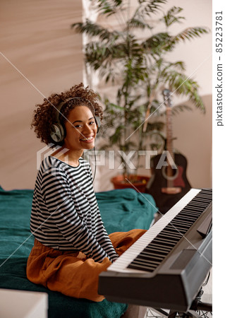 Joyful woman in headphones sitting near synthesizer at home Joyful woman in headphones sitting near synthesizer at home 85223781