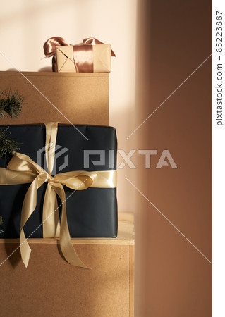 A lot of gift boxes made of beige paper and black, with a beige ribbon. On a paper background with a ray of sunlight on the boxes. High quality photo 85223887