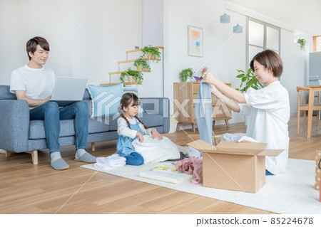 Mom and dad sitting on the couch and working on a computer with an elementary school girl helping to clean up clothes Mom and dad sitting on the couch and working on a computer with an elementary school girl helping to clean up clothes 85224678