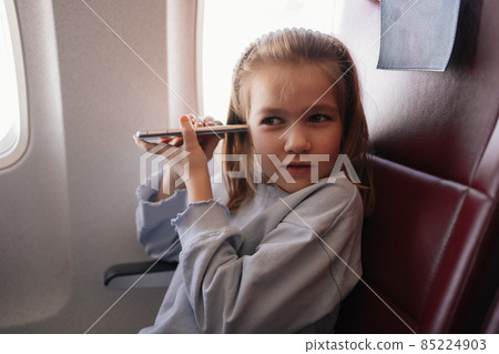 a little girl is talks hands-free calls on the phone in an airplane seat 85224903