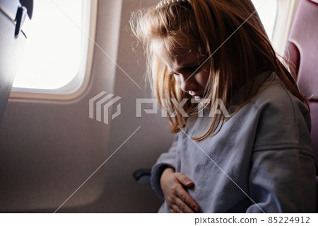 a little girl and holds the tummy because of the illness in an airplane  85224912