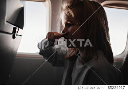 a little girl clamps nose because of unpleasant smell in airplane seat by window 85224917