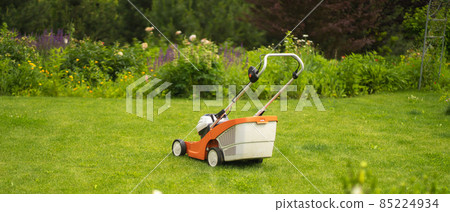 A lawnmower is at the beautiful green floral backyard lawn. A lawnmower is at the beautiful green floral backyard lawn. 85224934