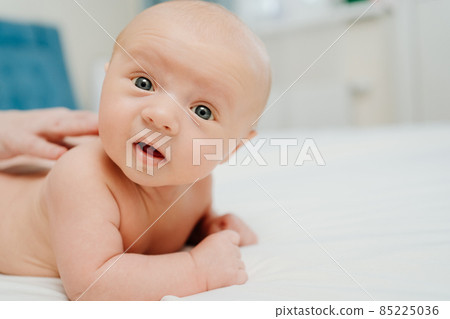 the baby lies on his tummy on a white sheet. and mom's hands massage the back. the baby lies on his tummy on a white sheet. and mom's hands massage the back. 85225036
