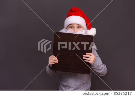 Santa holds an empty advertising board. santa boy on a gray background..copy space 85225217