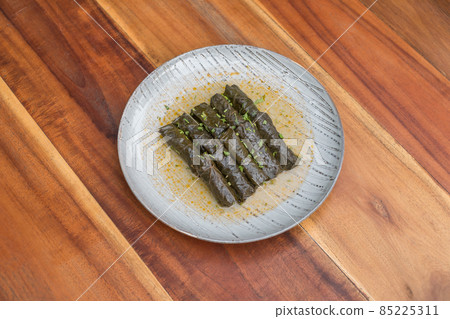 Delicious stuffed grape leaves. Traditional doom Mediterranean cuisine Dolma on white plate with fresh cilantro, on wooden background, close up.  85225311