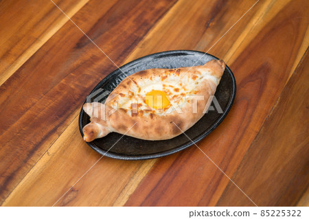 Traditional Georgian cuisine. Ajara khachapuri with egg on black plate on wooden background Top view, close up with copy space. High quality photo Traditional Georgian cuisine. Ajara khachapuri with egg on black plate on wooden background Top view, close up with copy space. High quality photo 85225322