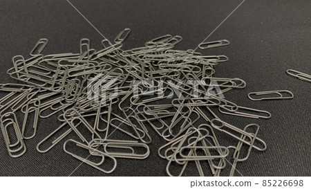 Lots of metal paper clips scattered across the black table Lots of metal paper clips scattered across the black table 85226698