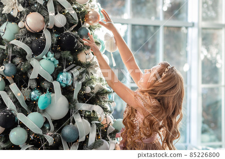 Cute little girl is decorating Christmas tree indoors. Merry Christmas and Happy Holidays concept. 85226800