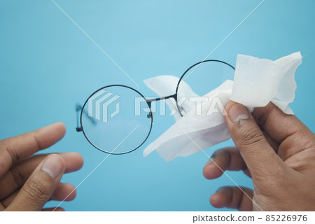 cleaning eyeglass with tissue close up  85226976