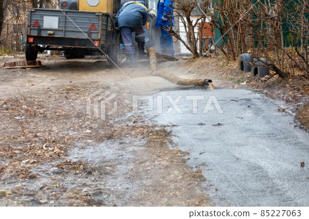 A team of communal workers uses a pump and a hose to pump out water from a manhole. 85227063
