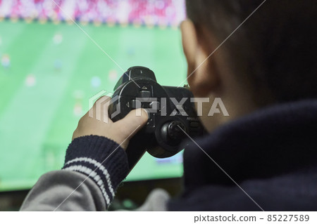 A little boy playing soccer on a gaming console. Cropped shot of a kid from behind, playing football game on wireless gamepad or joystick on his hands A little boy playing soccer on a gaming console. Cropped shot of a kid from behind, playing football game on wireless gamepad or joystick on his hands 85227589