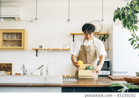 一個男人在廚房的紙板箱裡放著蔬菜 一個男人在廚房的紙板箱裡放著蔬菜 85230202