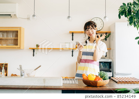 A woman holding a smartphone in the kitchen (smartphone / smile) A woman holding a smartphone in the kitchen (smartphone / smile) 85234149