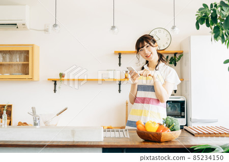一個女人在廚房裡拿著智能手機(智能手機/微笑) 一個女人在廚房裡拿著智能手機(智能手機/微笑) 85234150