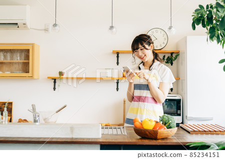 一個女人在廚房裡拿著智能手機(智能手機/微笑) 一個女人在廚房裡拿著智能手機(智能手機/微笑) 85234151