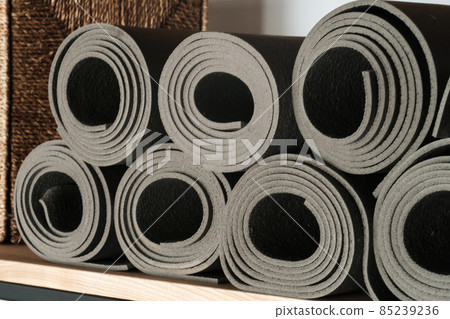 Gray yoga mats lying on a shelf, rolled up 85239236