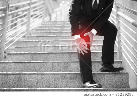 Businessman in a suit have the sore pain and painful knee problem expression and walk up and down on the stairway during go to office. Health care concept. Businessman in a suit have the sore pain and painful knee problem expression and walk up and down on the stairway during go to office. Health care concept. 85239293