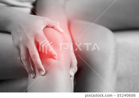 A woman suffering from feeling knee pain sitting sofa at home. hand massaging his painful knee. Health care and medical concept. 85240686